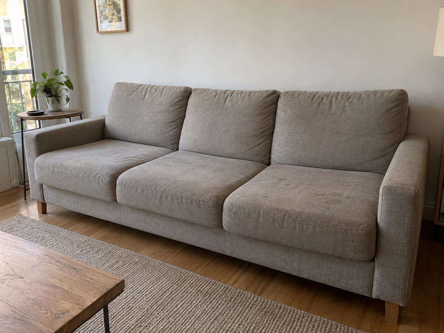 Three-seat grey-beige fabric sofa with signs of everyday use on the seats