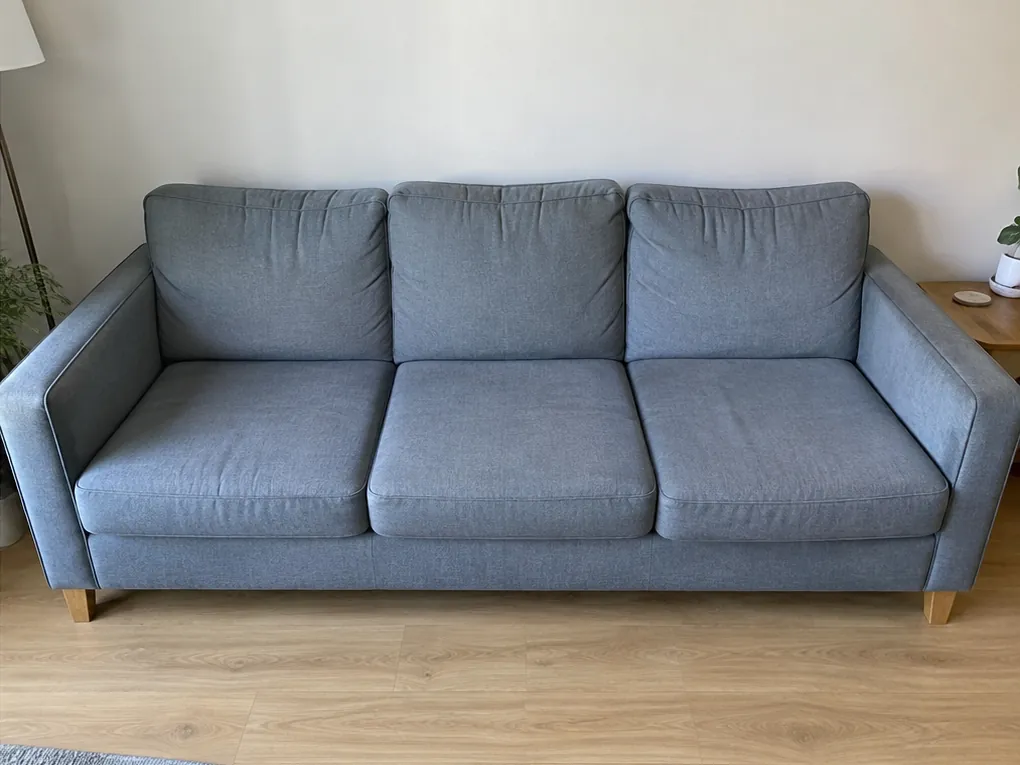 Illustrative after view: same blue-grey sofa with cleaned seats and unchanged creases